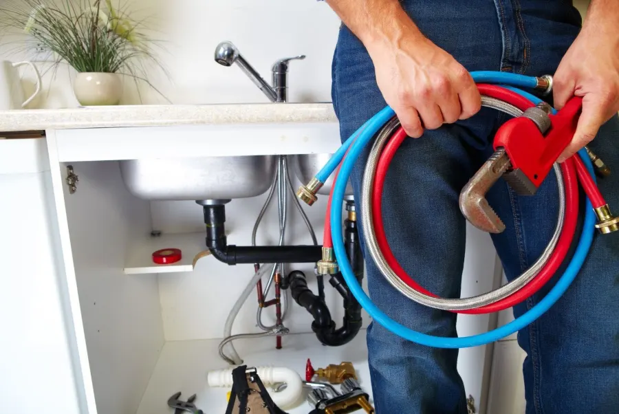 Plumber holding supply hoses and a pipe wrench